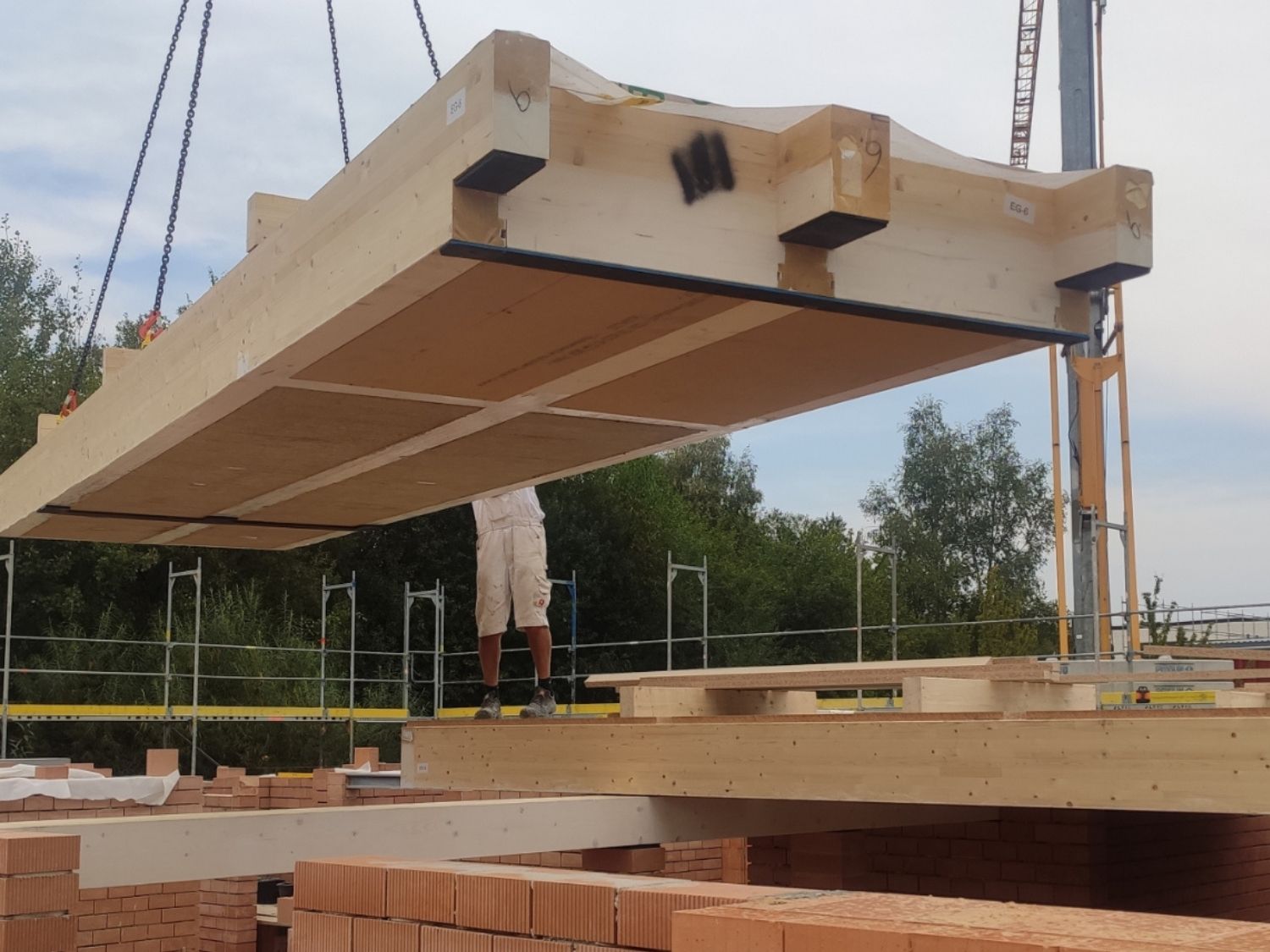 Ein Krank hebt ein Deckenelement aus Holz und Lehm auf eine Mauer aus Ziegeln.