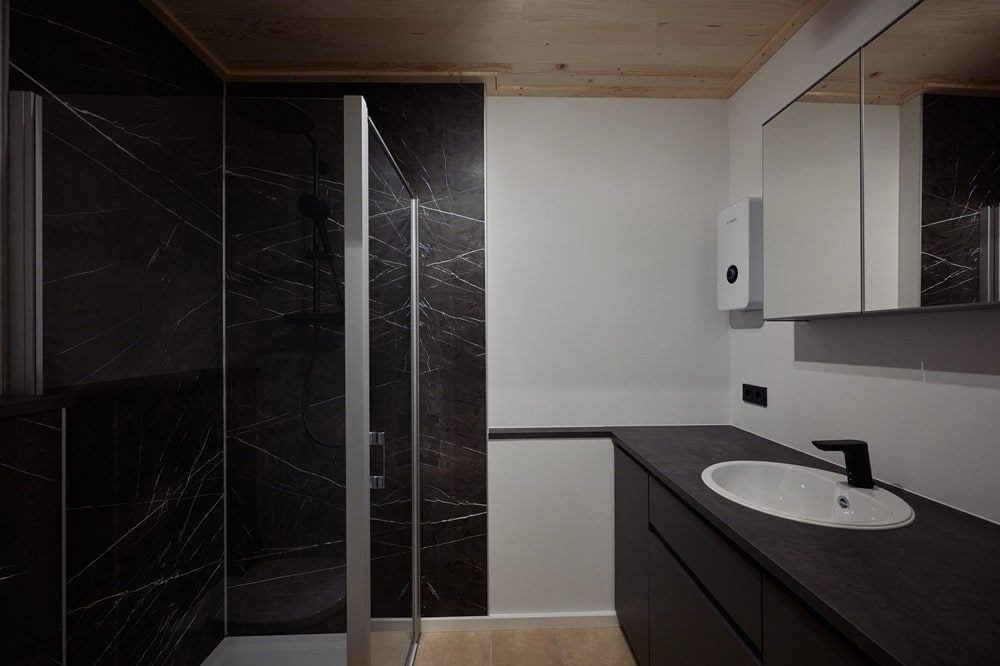 Modernes Badezimmer mit schwarzer Duschwand, Glasduschtür, weißem Waschbecken und schwarzer Armatur.