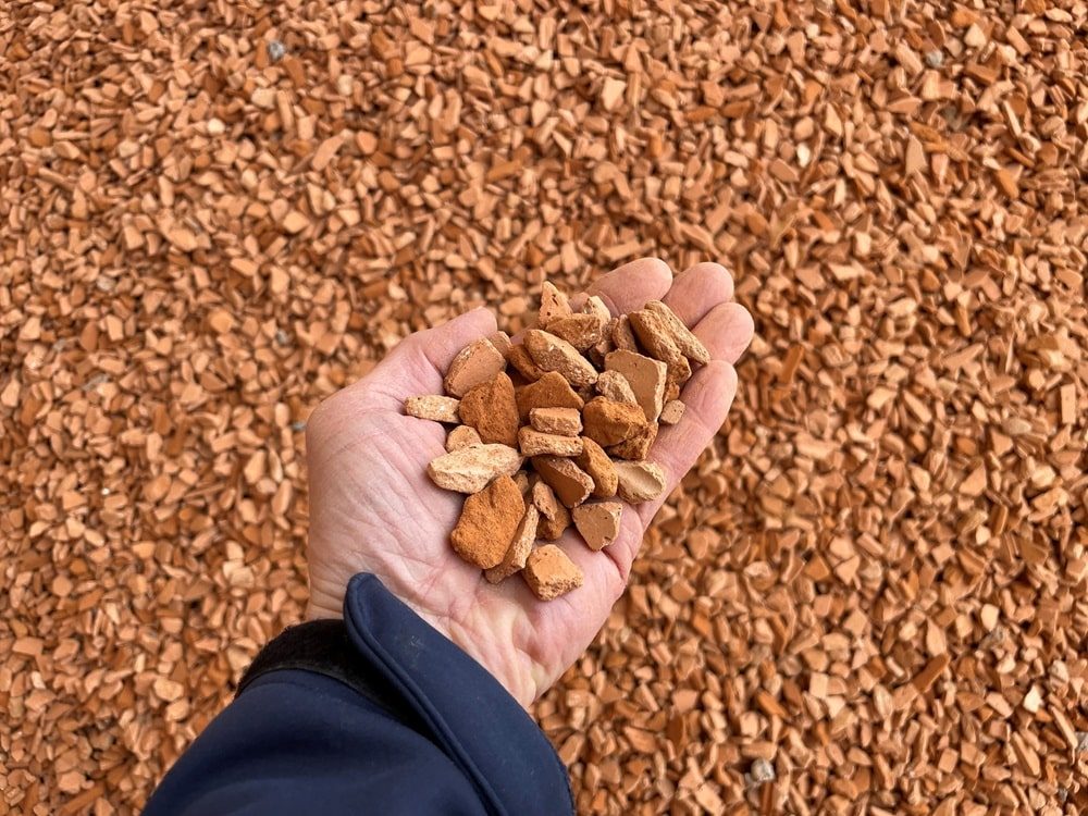 Hand hält mehrere kleine, braune Ton- oder Keramikstücke vor einem Hintergrund aus ähnlichem Material.