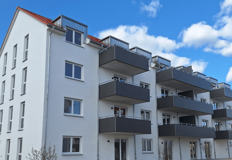Moderne Wohnanlage gebaut aus Silvacor Ziegelsteine mit weißen Fassaden, roten Satteldächern und mehreren Balkonen unter blauem Himmel in Kulmbach.