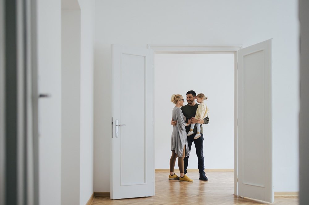 Familie mit Kind steht in leerer Wohnung mit offenem weißen Türrahmen.