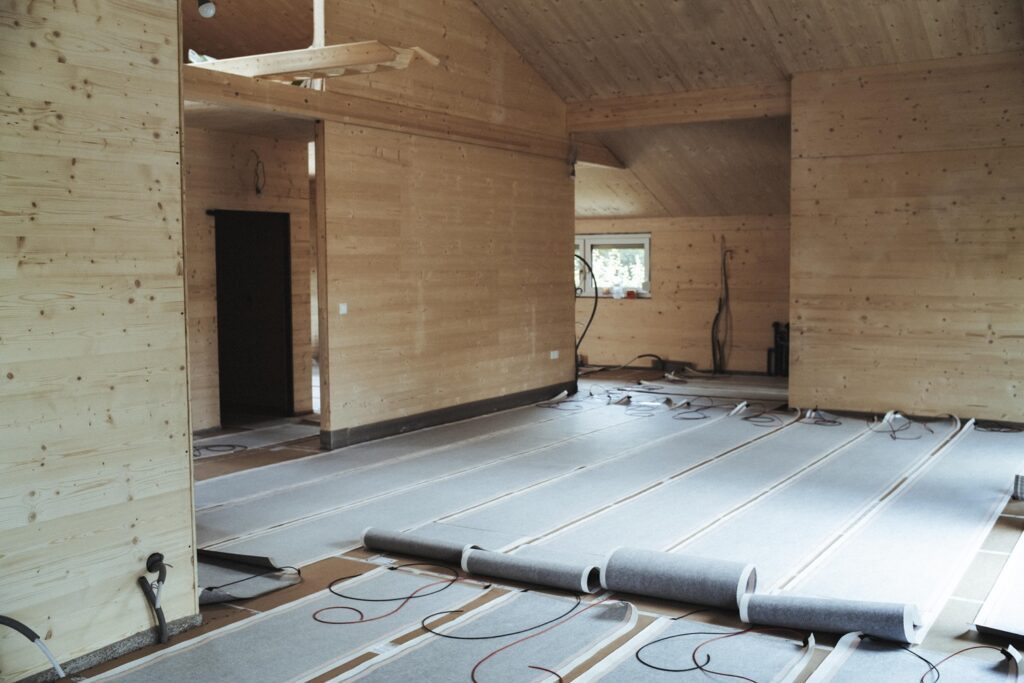 Innenraum eines Hauses mit sichtbaren Holzwänden und installierter Fußbodenheizung mit Heizpapier auf dem Boden.