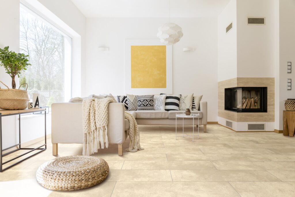 Helles Wohnzimmer mit beige Designestrichziegel Samir, grauem Sofa mit gemusterten Kissen, Kamin und großem Fenster.