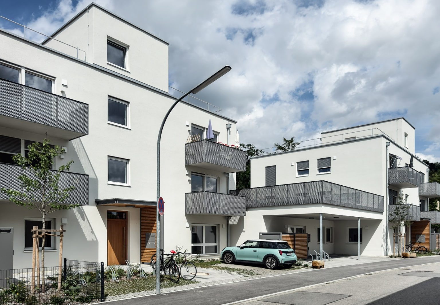 Hybrid genutzter Neubau in Landshut mit weißer Fassade, mehreren Balkonen, geparktem Auto und Fahrrädern vor dem Gebäude.