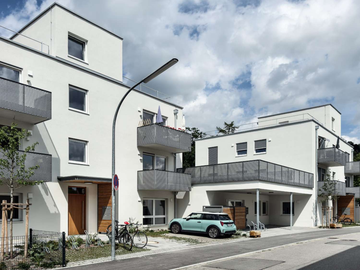 Hybrid genutzter Neubau in Landshut mit weißer Fassade, mehreren Balkonen, geparktem Auto und Fahrrädern vor dem Gebäude.