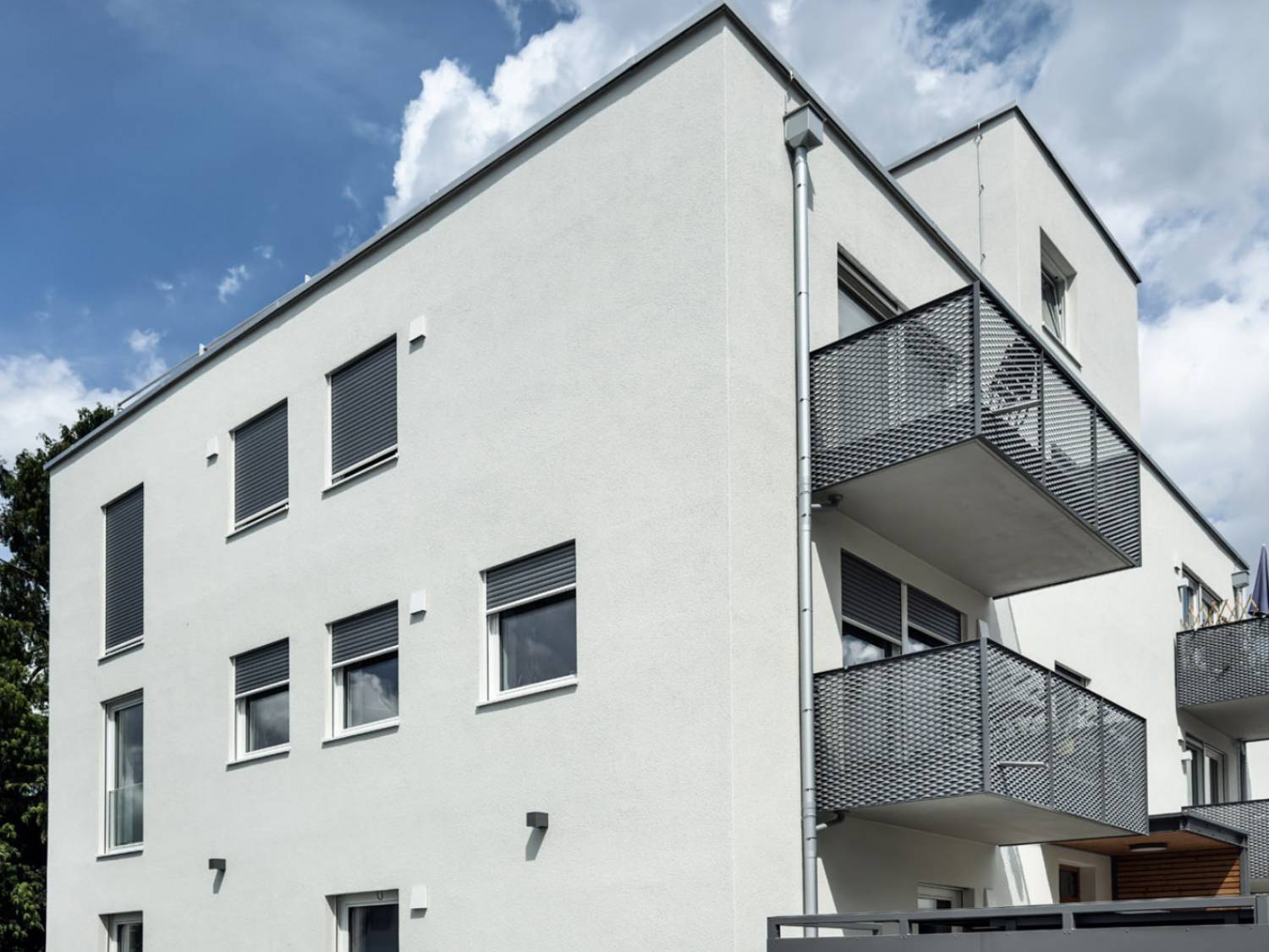 Seitenansicht eines hybrid genutzten Neubaus in Landshut mit weißer Fassade, mehreren Fenstern und drei Balkonen mit Metallgeländern.