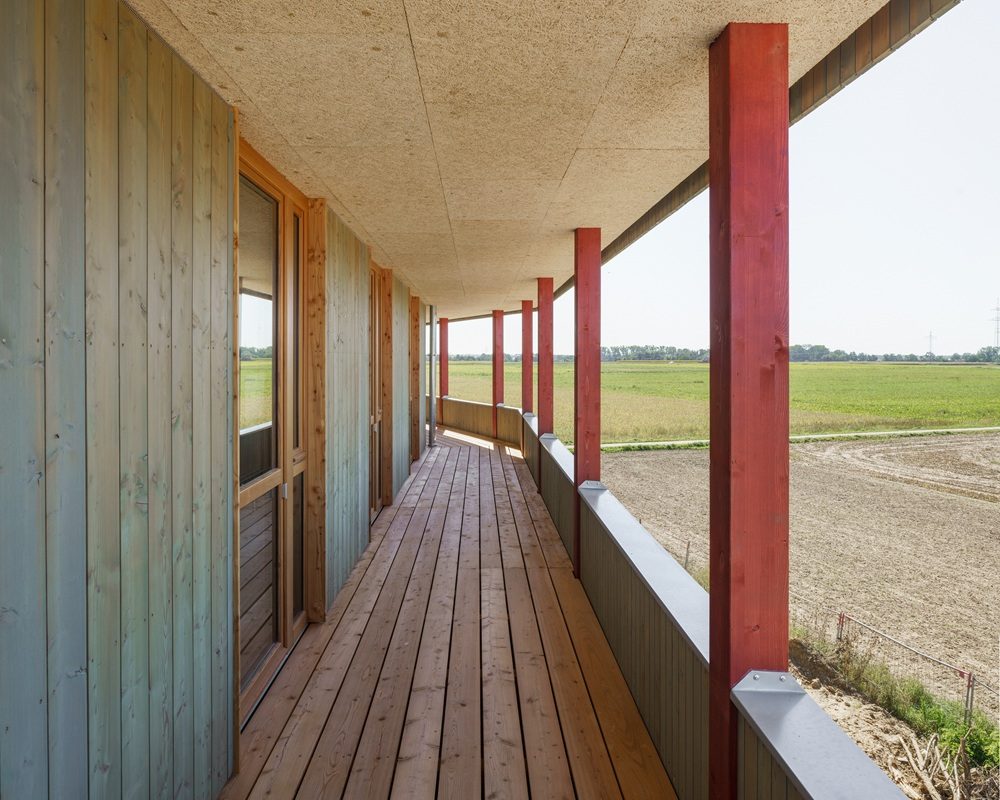 Haus fast ohne Heizung in Ingolstadt: Langer Balkon mit Holzfußboden und Holzverkleidung an der Hauswand, rot gestrichene Stützen, Blick auf offene Felder in Ingolstadt.