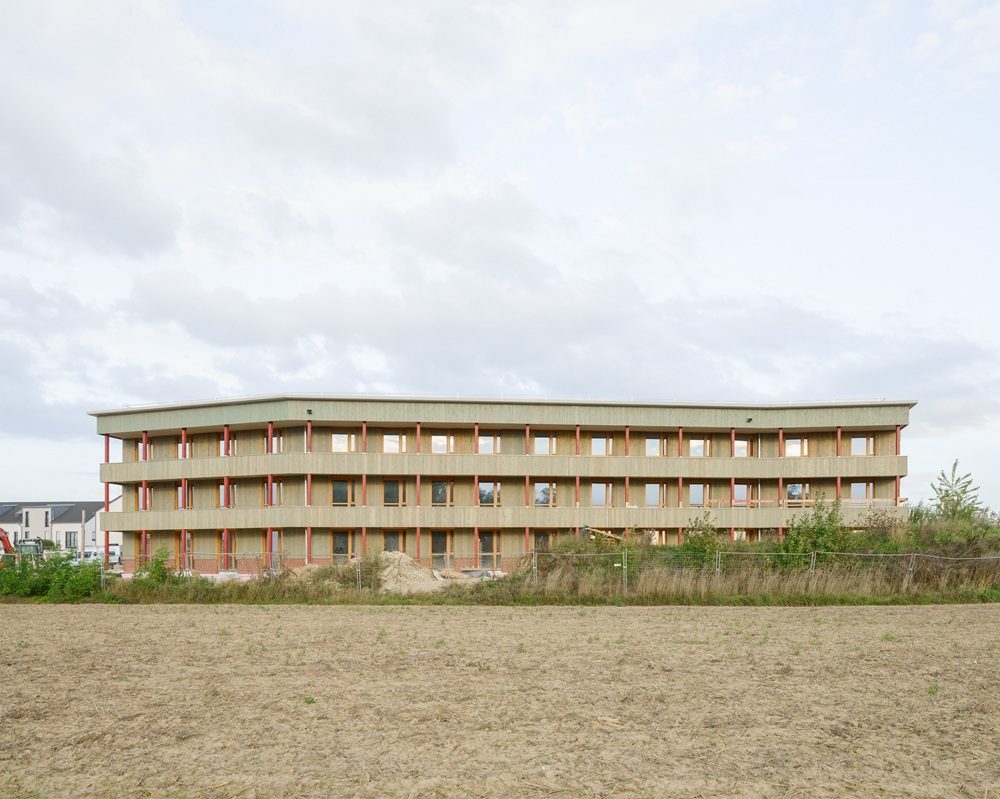 Haus fast ohne Heizung in Ingolstadt: Mehrstöckiges Wohngebäude mit Holzfassade und Balkonen, umgeben von unbebautem Gelände, unter bewölktem Himmel in Ingolstadt.