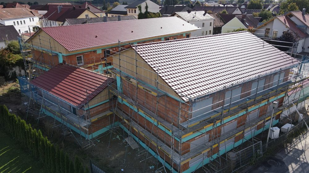 Leipfinger-Bader ZIEGELMODULE: Zwei Gebäude mit roten Ziegeldächern in Bauphase, umgeben von Gerüsten, in einem Wohngebiet in Laberweinting.