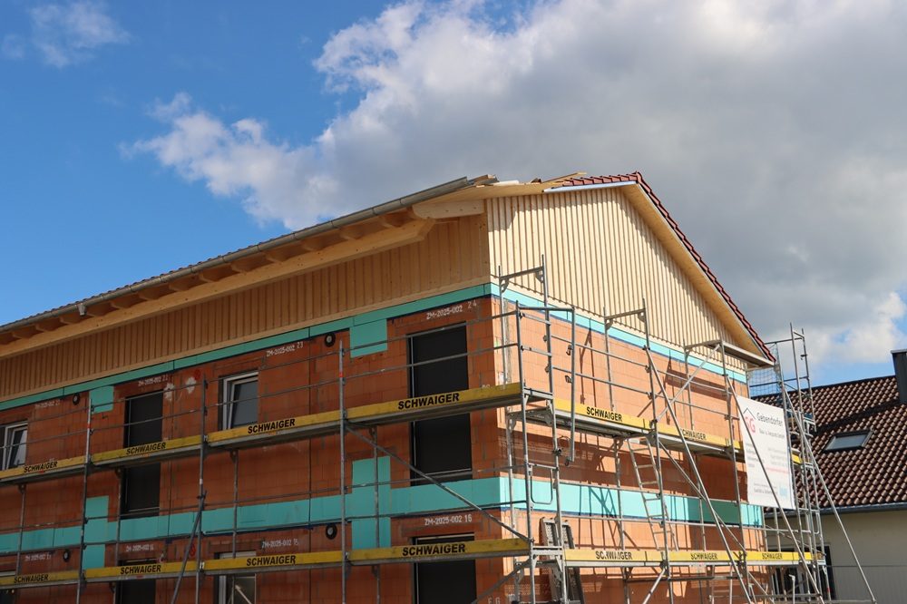 Leipfinger-Bader ZIEGELMODULE: Haus im Rohbau mit Holzverschalung und Gerüst mit Aufschrift 'SCHWAIGER' vor blauem Himmel mit Wolken.