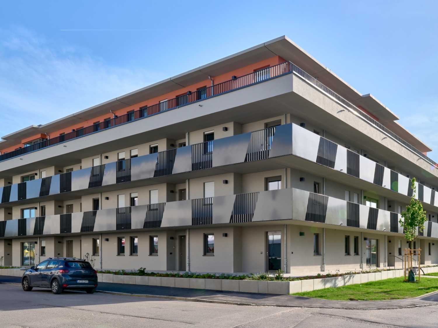 Moderner mehrstöckiger Wohnblock mit Balkonen und parkendem Auto davor.