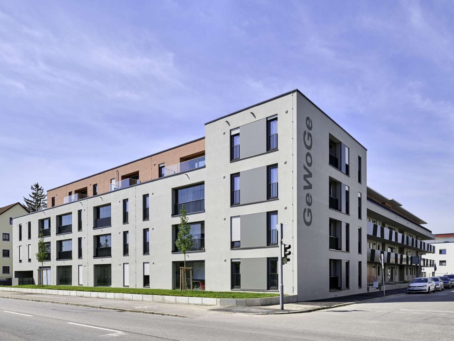 Modernes, mehrstöckiges Wohngebäude mit Balkonen und großem Schriftzug 'GeWoGe' an der Ecke, Straße im Vordergrund.