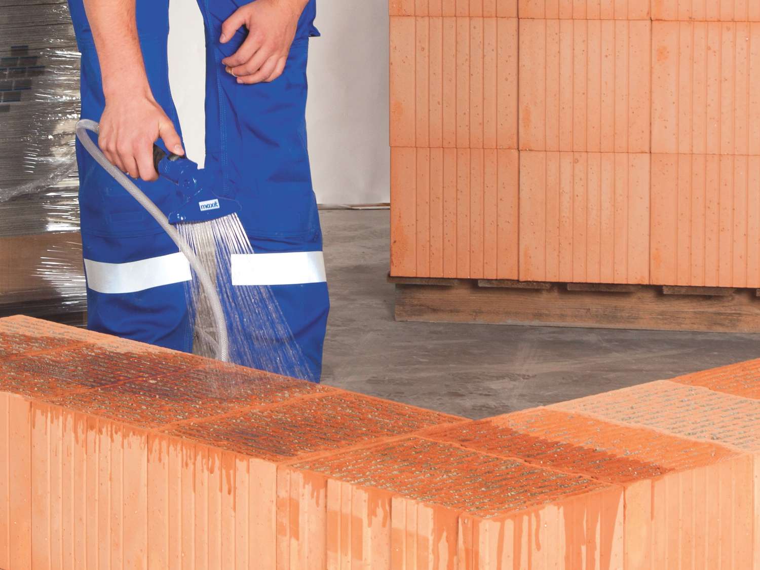 Person in blauer Arbeitskleidung gießt Wasser auf eine Ziegelmauer.