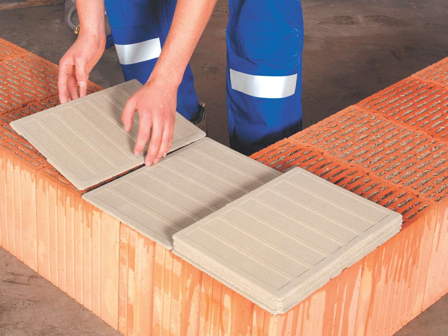 Hände legen zwei graue Maxit Mörtelpads Eco auf eine Mauer aus roten Ziegelsteinen.