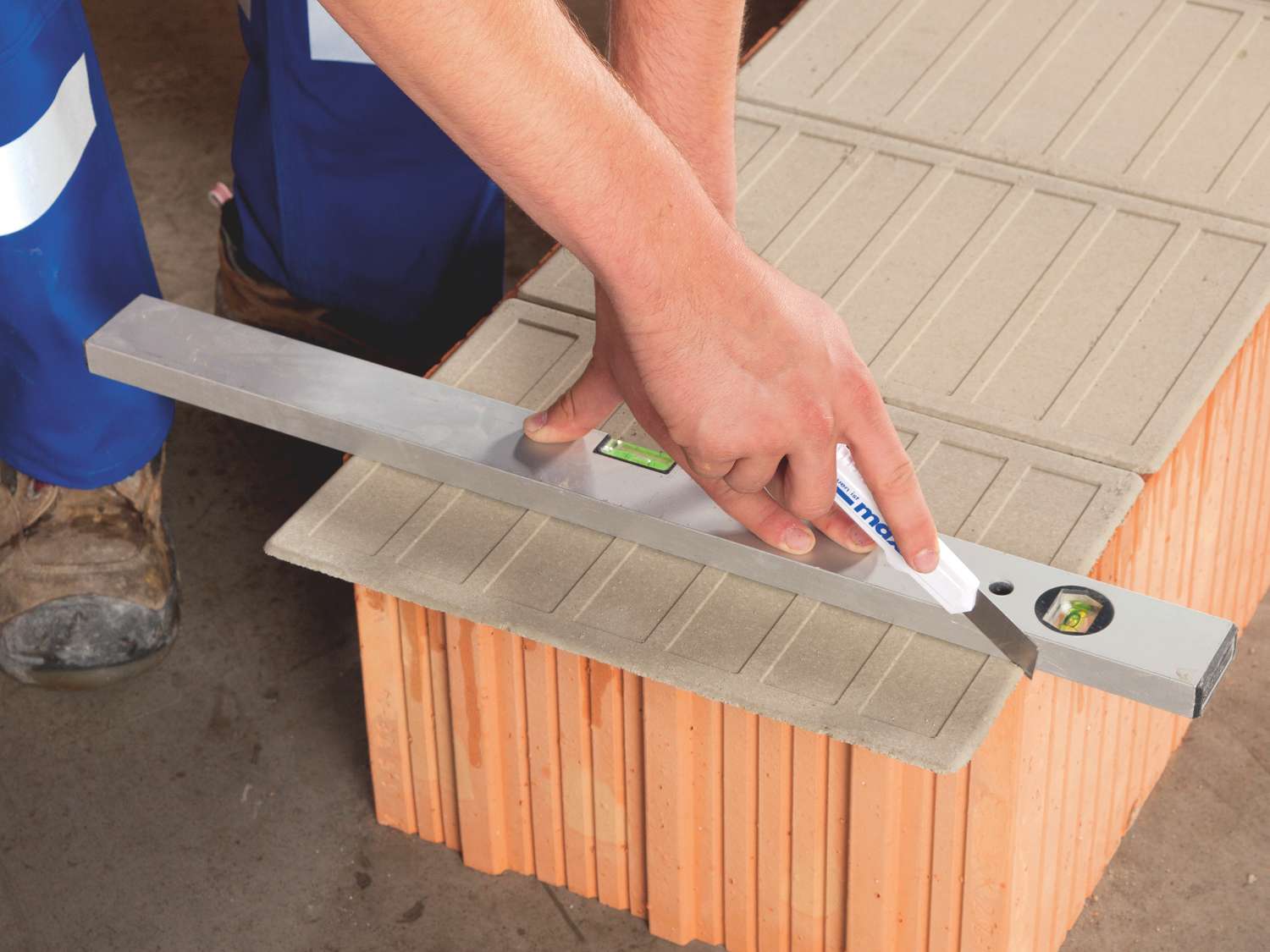 Hand misst mit Wasserwaage und Maxit Mörtelpad Eco die Ebenheit einer Ziegelsteinreihe.