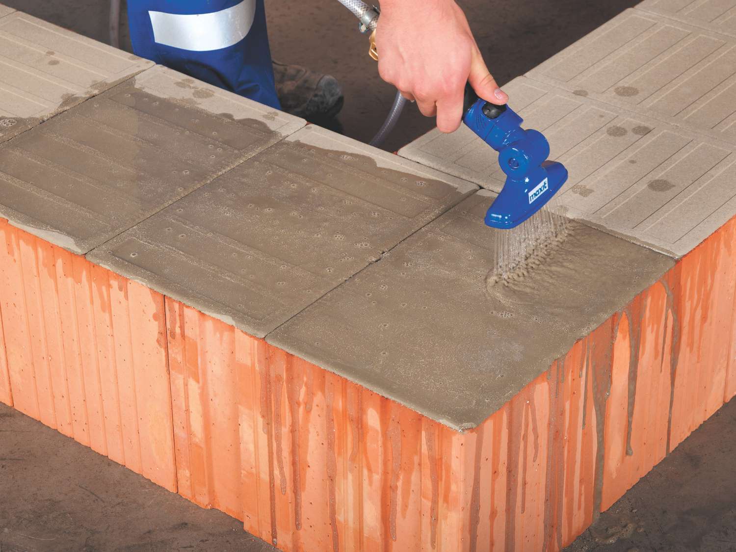 Hand sprüht Wasser auf Maxit Mörtelpad Eco auf eine Ziegelsteinreihe.