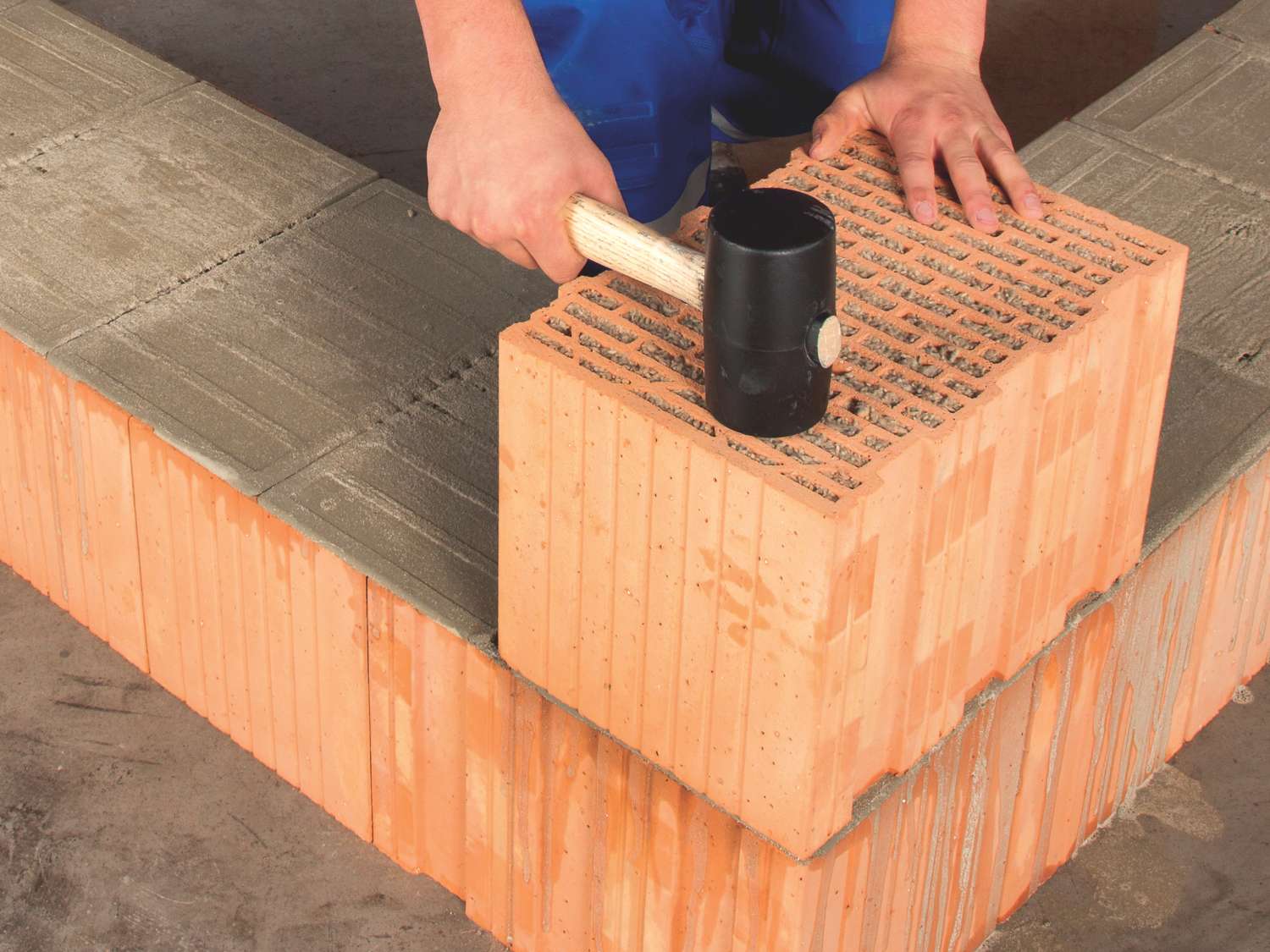 Hände eines Bauarbeiters schlagen mit einem Gummihammer auf einen Ziegelstein, der auf einem Maxit Mörtelpad Eco liegt.