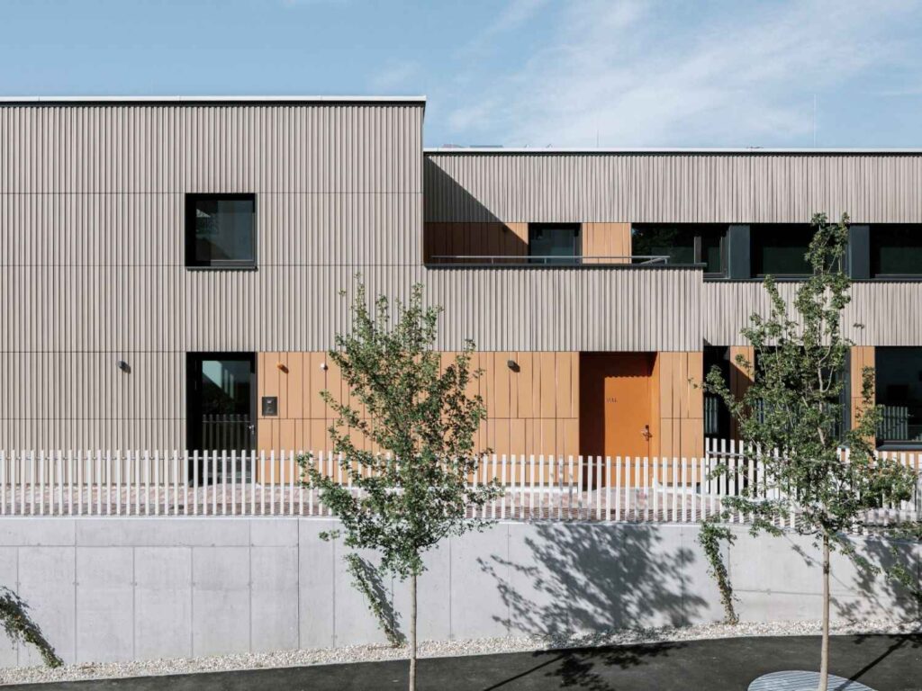 Modernes Pfarrzentrum mit Tonality® Keramikfassade, rechteckigen Fenstern, Holzelementen und weißem Zaun im Vordergrund.