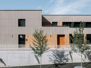 Modernes Pfarrzentrum mit Tonality® Keramikfassade, rechteckigen Fenstern, Holzelementen und weißem Zaun im Vordergrund.