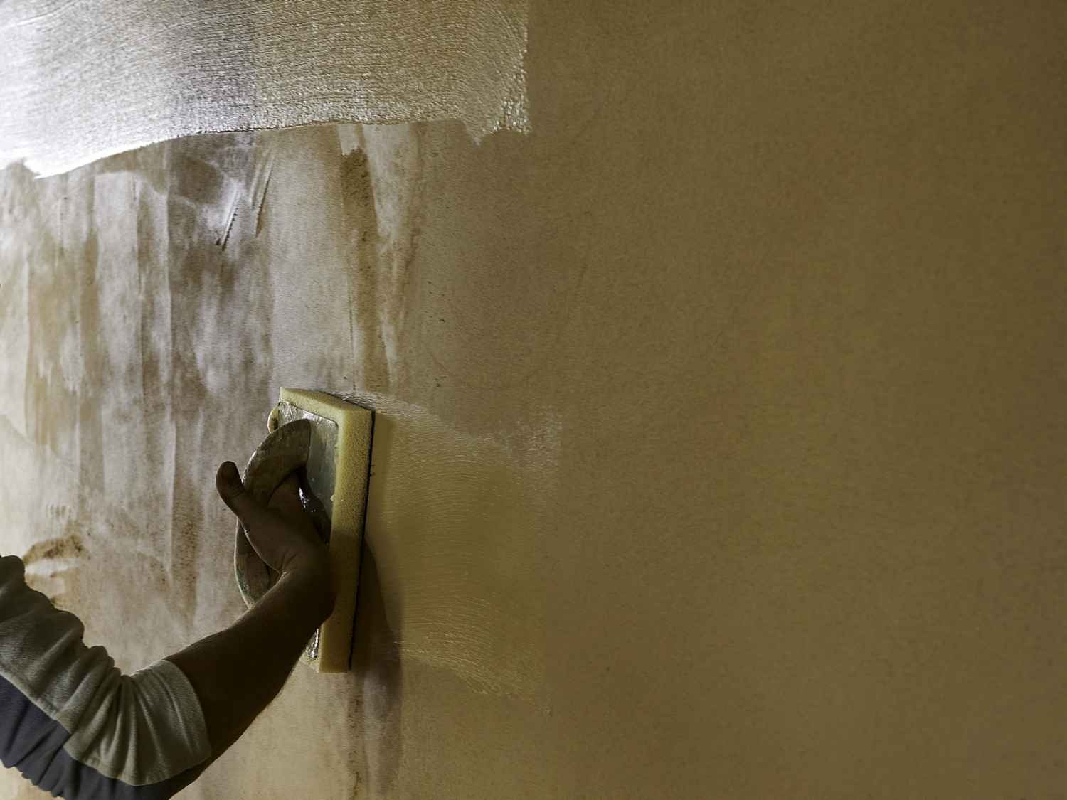Hand mit Handschuh trägt Lehmputz von Leipfinger-Bader mit Glättkelle auf eine Wand auf.