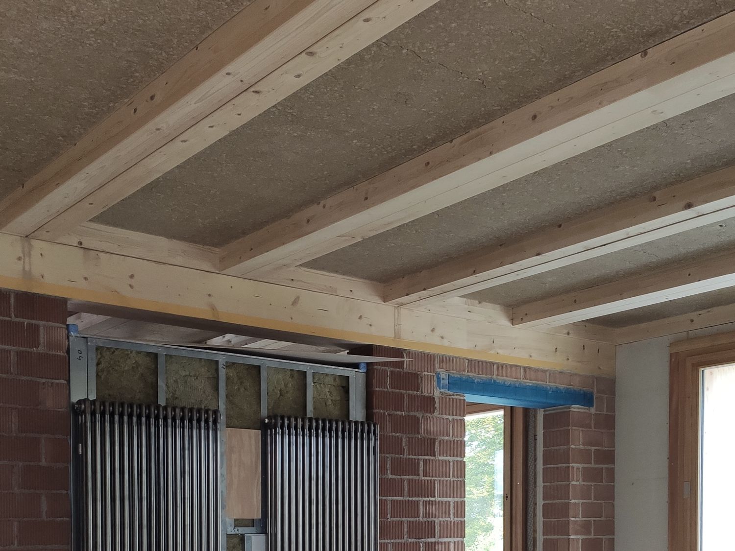 Leipfinger-Bader Holz-Lehm Massivdecke mit sichtbaren Holzbalken und Ziegelwand im Forschungshaus 5 in Bad Aibling.