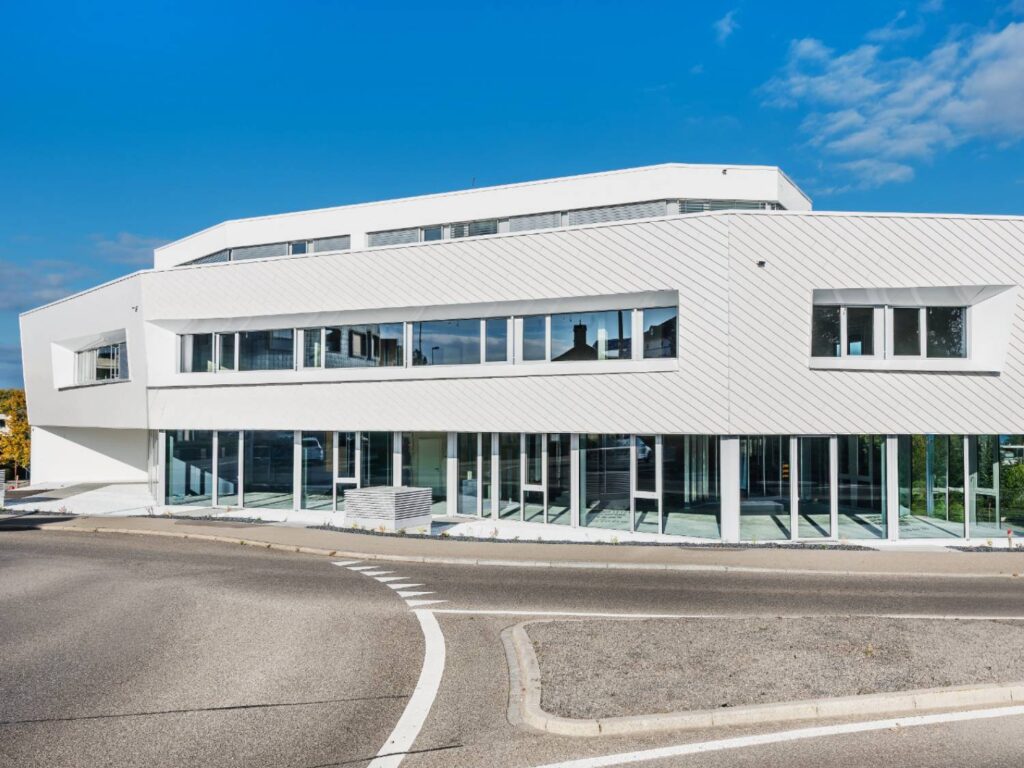 Modernes Gebäude mit polygonaler Form und weißer TONALITY® Keramikfassade in Stülpoptik mit großen Fenstern und flachem Dach.