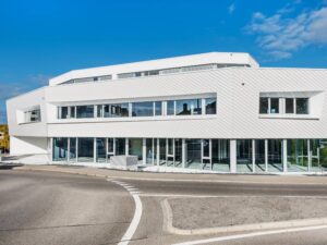 Modernes Gebäude mit polygonaler Form und weißer TONALITY® Keramikfassade in Stülpoptik mit großen Fenstern und flachem Dach.