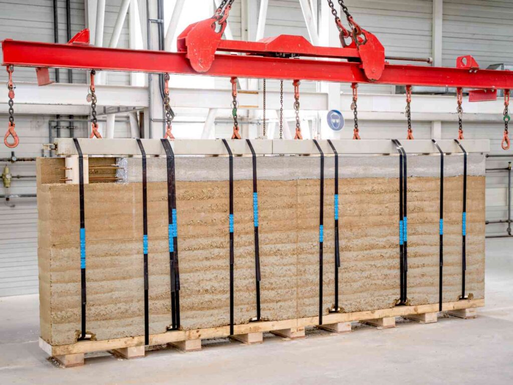 Stampflehmwand, mit schwarzen Gurten gesichert, auf Holzpalette in Produktionshalle.