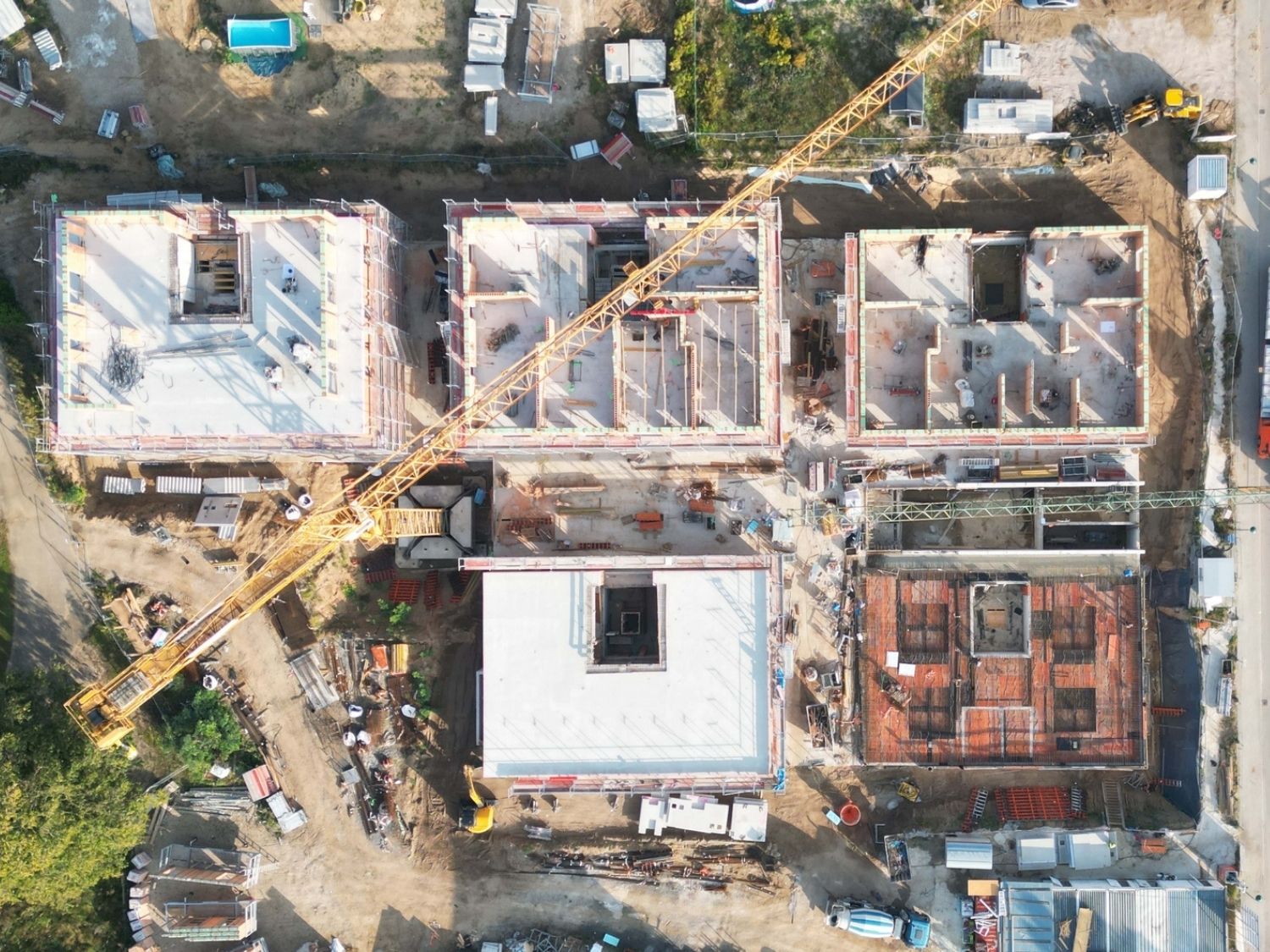 Luftaufnahme einer Wohnanlage in Werneuchen im Bau mit mehreren rechteckigen Gebäuden, Baukran und Baumaterialien auf dem Gelände.