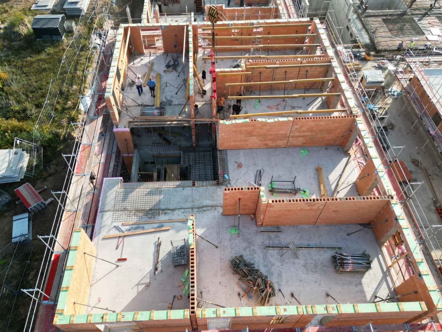 Luftaufnahme einer Baustelle mit Ziegelfertigteilen für eine Wohnanlage in Werneuchen, auf der mehrere Wände und Räume im Rohbau sichtbar sind.