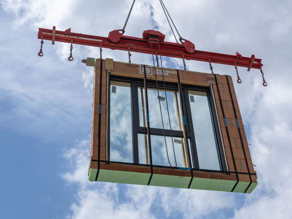 Ziegelfertigteil von Leipfinger-Bader mit Fensterzarge hängend im Kran.